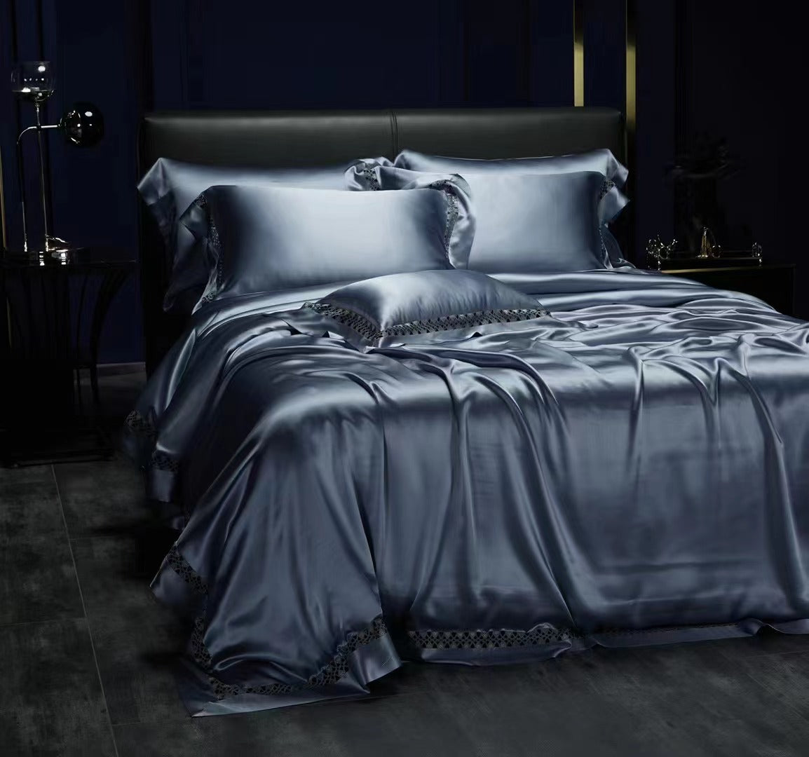 A luxurious bedroom with a dark color scheme, featuring a bed with a satin comforter and matching pillows, a black headboard, and a nightstand with a lamp.
