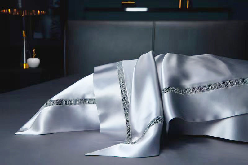 a luxurious white silk bedding set with silver rhinestones or crystals, placed on a dark surface.