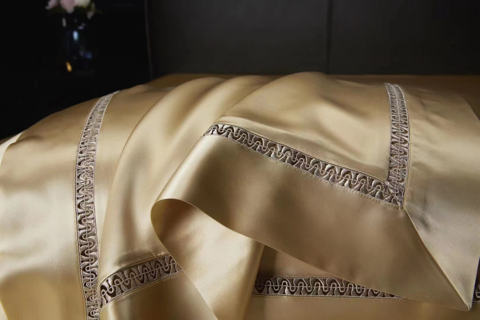 A close-up view of a luxurious gold-colored fabric, possibly silk or satin, with intricate embroidered patterns along the edges.