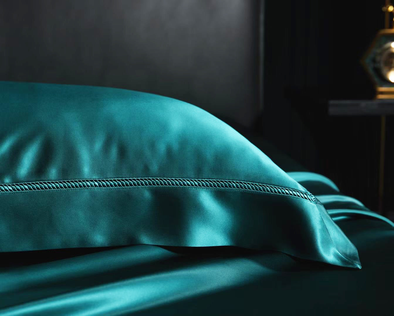 A close-up view of a teal-colored pillowcase or duvet cover resting on a bed, with a dark background.