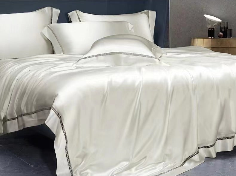 A luxurious white bed with a satin comforter and matching pillows, set against a dark background.