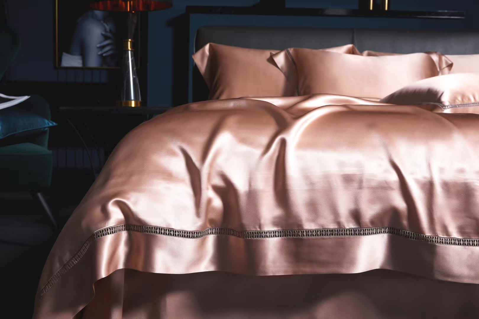 A luxurious bed with a pink satin comforter and matching pillows, set against a dark background.