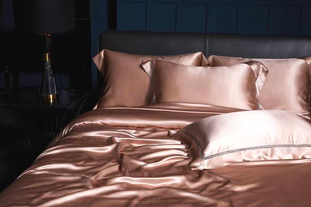A luxurious bed with a satin comforter and matching pillows, set against a dark blue wall.