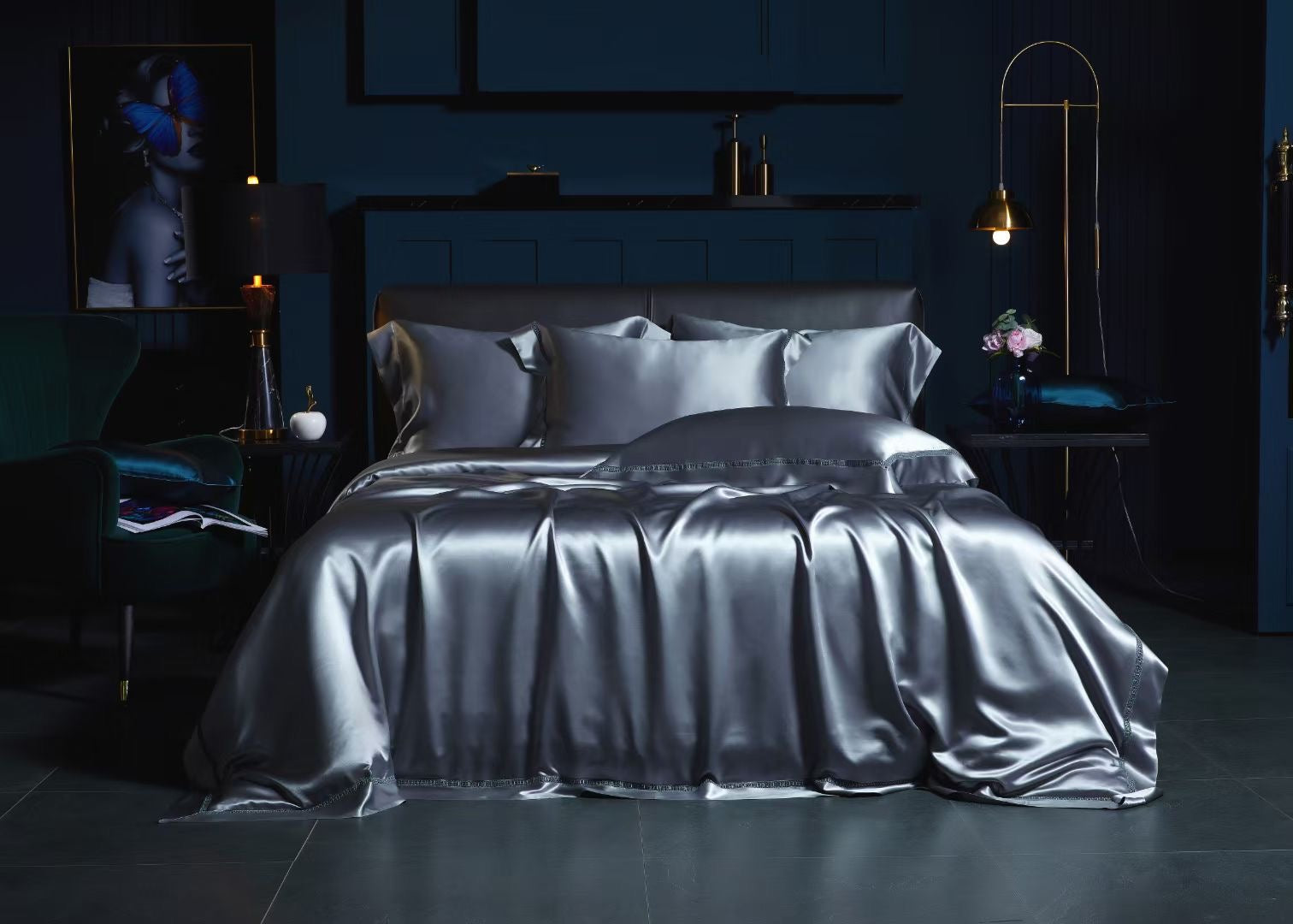 a luxurious bedroom with a large bed dressed in a satin bedspread and matching pillows. The room has dark blue walls, a black leather headboard, and a gold lamp on a side table. There is also a framed image of a woman on the wall.