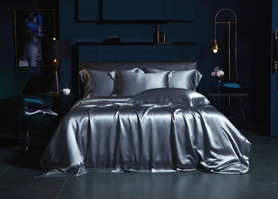 a luxurious bedroom with a large bed dressed in a satin bedspread and matching pillows. The room has dark blue walls, a black leather headboard, and a gold lamp on a side table. There is also a framed image of a woman on the wall.