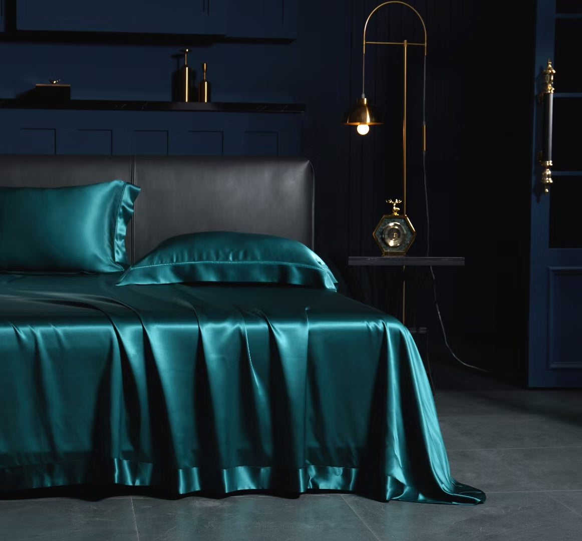 A luxurious bedroom with a dark blue color scheme, featuring a bed with a satin bedspread and matching pillows, a nightstand with a lamp, and a gold-colored lampshade.