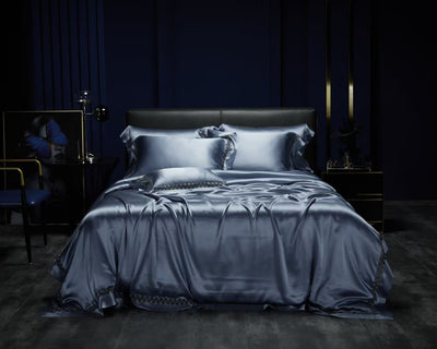 a luxurious bedroom with a large bed dressed in a satin blue bedding set, including a duvet cover and pillows. The room has dark blue walls and a dark wooden floor, creating a sophisticated and elegant atmosphere.