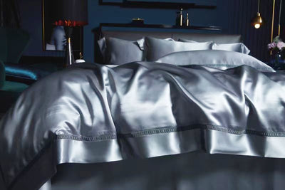a luxurious bedroom with a large bed covered in a satin comforter and pillows. The bed is set against a dark blue wall, creating a sophisticated and elegant atmosphere.