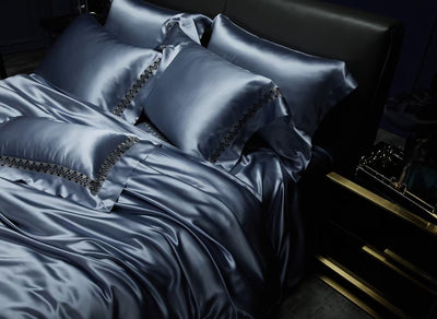 A luxurious bed with a satin comforter and matching pillows, set against a dark background.