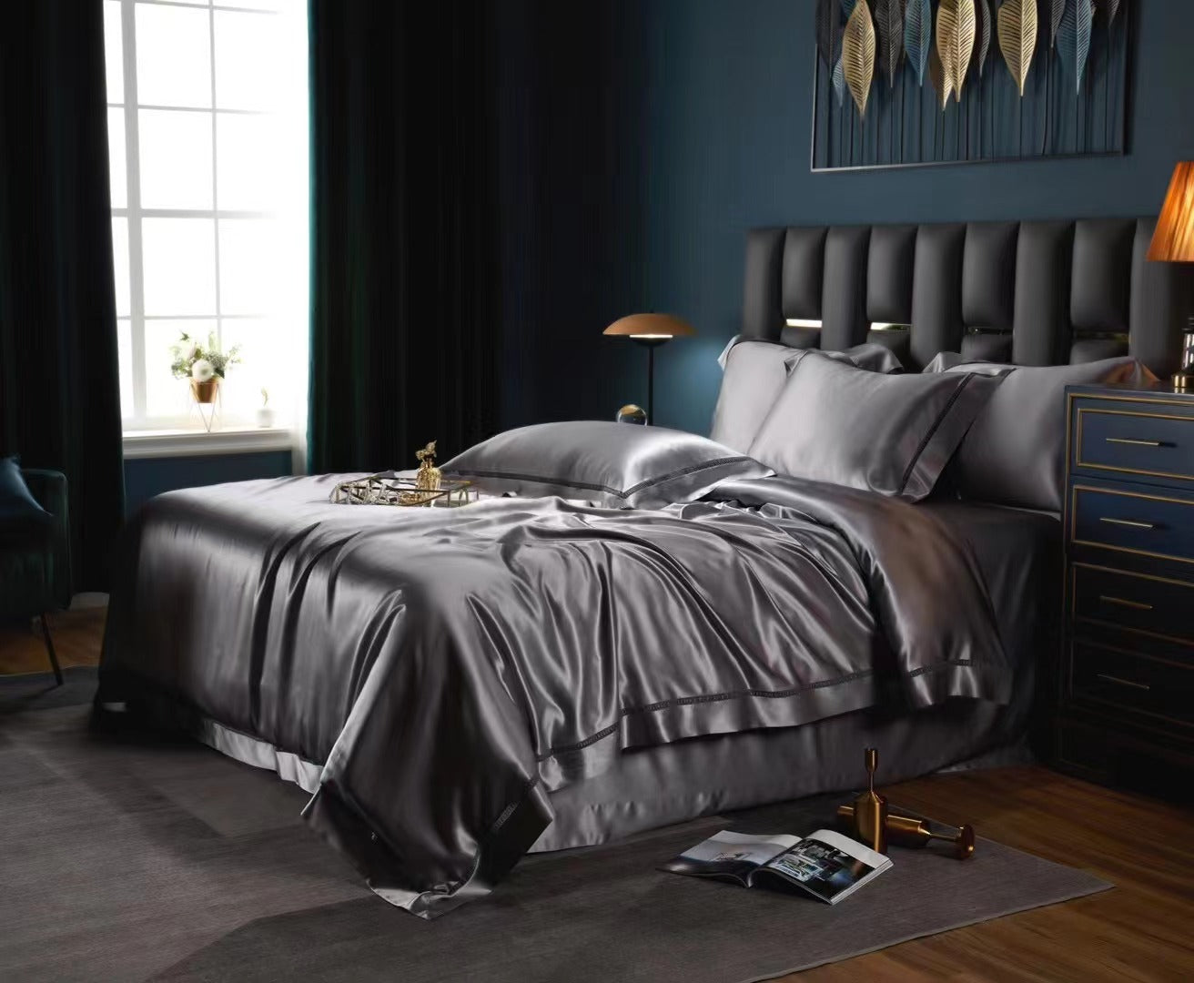 a luxurious bedroom with a large bed, dark blue walls, and a window. The bed is covered in a satin-looking comforter and pillows, creating an elegant and sophisticated atmosphere. There is also a lamp and a vase on the bed, adding to the room's decor.