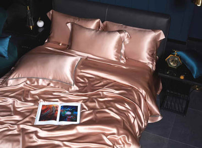 a luxurious bedroom with a bed covered in a satin comforter and matching pillows. There is a nightstand next to the bed with a clock and a lamp. On the bed, there is a book with an open cover, and a small decorative item is placed on the nightstand.