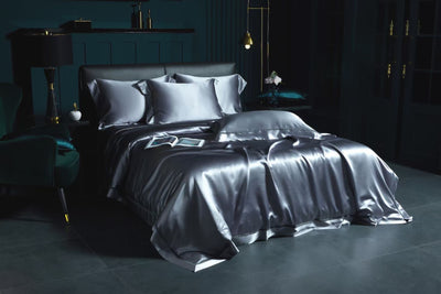 a luxurious bedroom with a large bed dressed in a satin bedding set, including a gray comforter and matching pillows. The room has dark green walls and a dark wood floor, creating a sophisticated and elegant atmosphere.