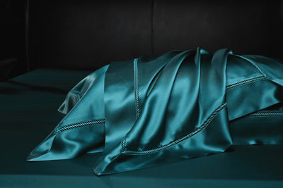 A close-up view of a dark green satin fabric, possibly a pillowcase or duvet cover, with a dark background.