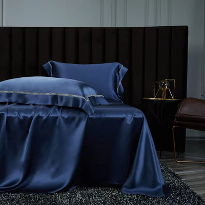a luxurious bedroom with a large bed dressed in a blue satin bedspread and matching pillows. The bed is set against a dark headboard, creating a striking contrast. A small side table is positioned next to the bed, and a gold-colored lamp is placed on the table. The overall scene conveys a sense of elegance and sophistication.