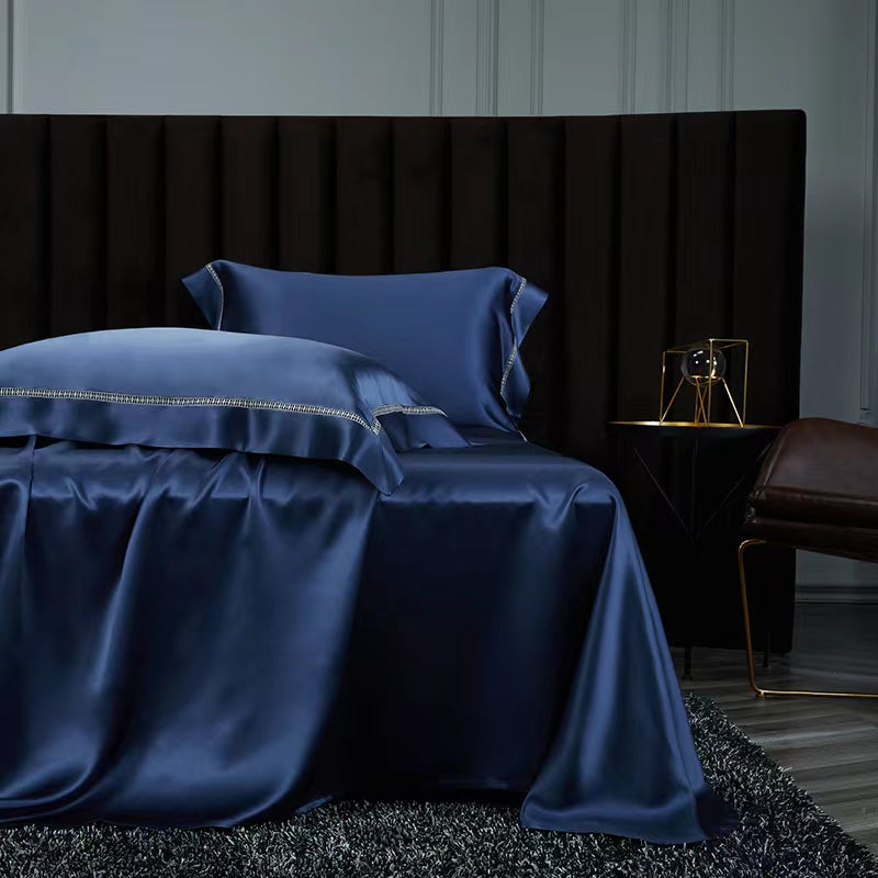 a luxurious bedroom with a large bed dressed in a blue satin bedspread and matching pillows. The bed is set against a dark headboard, creating a striking contrast. A small side table is positioned next to the bed, and a gold-colored lamp is placed on the table. The overall scene conveys a sense of elegance and sophistication.