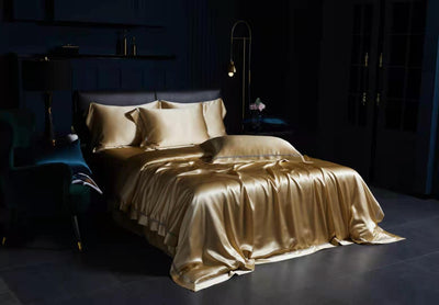 a luxurious bedroom with a large bed dressed in a gold satin bedspread and matching pillows. The room has dark blue walls and a dark floor, creating a sophisticated and elegant atmosphere.