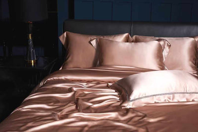 A luxurious bed with a satin comforter and matching pillows, set against a dark blue wall.