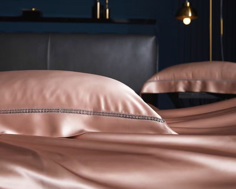 A close-up view of a bed with a pink pillow and a black headboard, set against a dark background with a lamp.