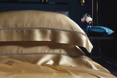 A close-up view of a bed with gold-colored bedding, including pillows and a blanket, against a dark background.