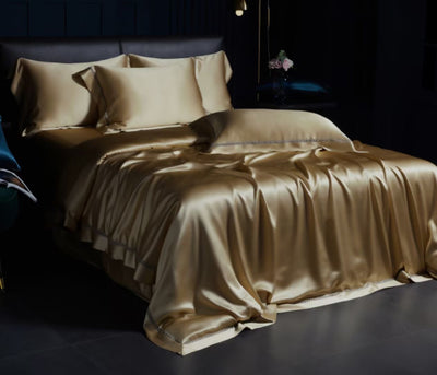 A luxurious gold-colored bed with a satin comforter and matching pillows, set against a dark background.