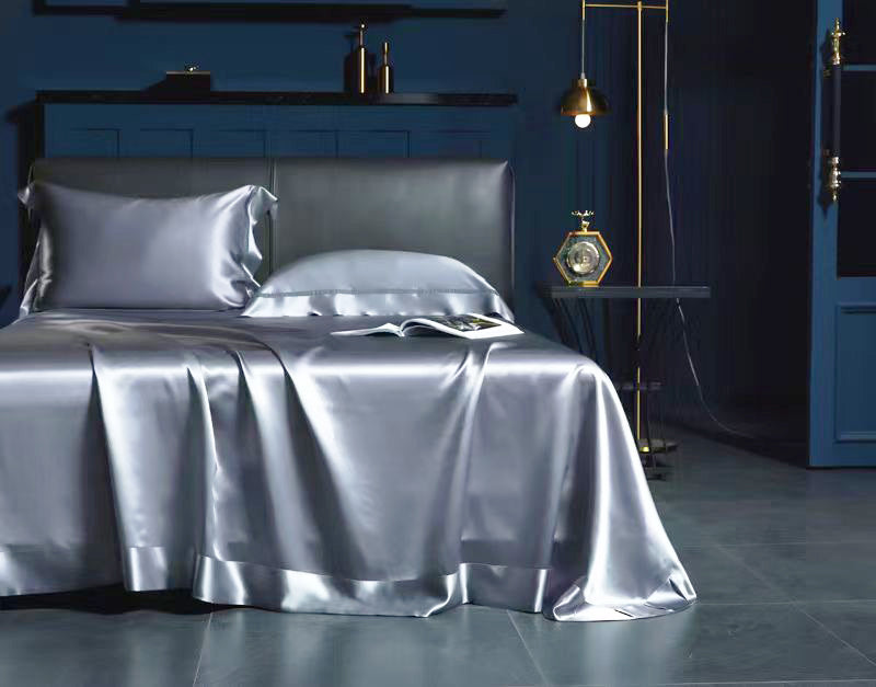 a luxurious bedroom with a bed dressed in a satin bedspread and matching pillowcases, creating a sense of elegance and sophistication. The room has a dark blue color scheme, with a black headboard and a gold pendant light hanging above the bed. The overall atmosphere of the room is calm and inviting, with a focus on comfort and style.